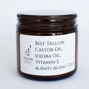 May include: A brown glass jar with a dark brown lid and a white label. The label reads "BEEF TALLOW, CASTOR OIL, JOJOBA OIL, VITAMIN E. & ANTI-AGING OILS". The jar contains a skincare product.