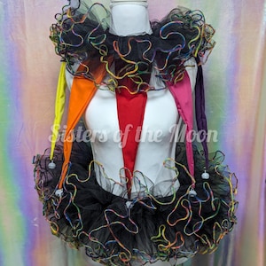 May include: A jester-style costume set featuring a black tulle ruffled collar and skirt with iridescent rainbow-colored edges. The outfit includes five long, pointed fabric drapes in yellow, orange, red, pink, and purple, each tipped with a small white bell.