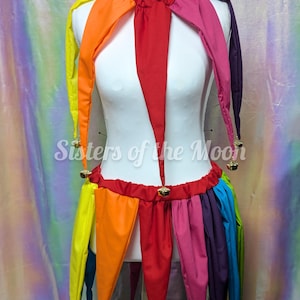 May include: A multi-colored jester costume featuring a collar and skirt with pointed fabric panels in yellow, orange, red, pink, purple, and blue. Each point is adorned with a small metallic bell. The garment is displayed on a white mannequin.