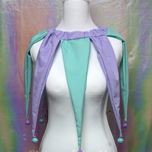 May include: A jester-style collar featuring alternating lavender and mint green fabric points. Each point is finished with a small matching bell at the tip. The collar is displayed on a white mannequin, with the text Sisters of the Moon visible.