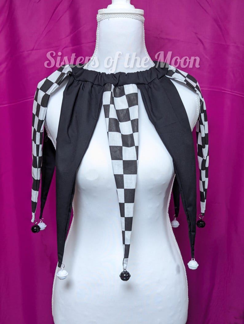 May include: A black and white checkered jester collar with long, pointed ends. The collar is black with a checkered pattern on the edges and center. Small bells hang from the tips. The text "Sisters of the Moon" is visible.