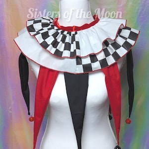 May include: A jester costume collar and neckpiece with a checkered pattern, red trim, and dangling black and red accents. The text "Sisters of the Moon" is visible on the collar.