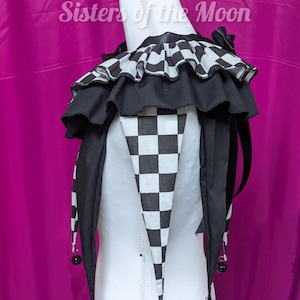 May include: A black and white jester collar with a checkered design and ruffled trim. The collar features long, pointed ends with small bells. The text "Sisters of the Moon" is visible in the background.
