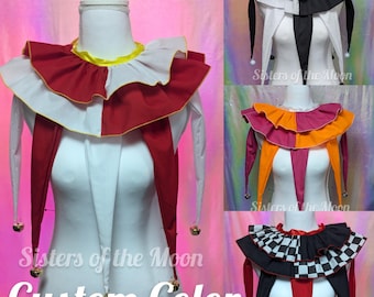 May include: A multi-layered ruffled collar featuring long pointed drapes and small metallic bells at the tips. The collar is displayed in various color combinations including red and white, black and white, orange and pink, and a black and white checkered pattern.