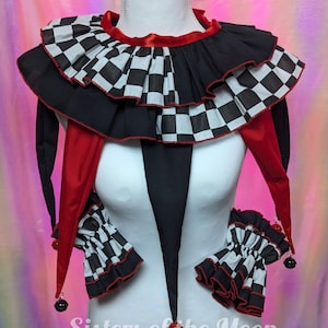 Peut inclure: Un ensemble col et poignets de style bouffon avec un motif à damier noir et blanc et une bordure rouge. Le col présente des volants superposés et de longues pointes en tissu rouge. Les poignets sont à volants avec des carreaux noirs et blancs.