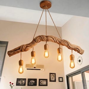 Peut inclure: Un luminaire de plafond composé d'un grand morceau de bois flotté incurvé suspendu par des cordes. Cinq ampoules avec des douilles en bois pendent à des longueurs variables du bois, diffusant une lueur chaude. Fixé par une rosace en bois.