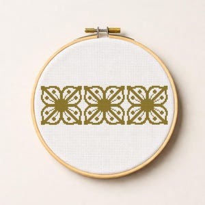 Op de afbeelding: Een voltooid kruissteekproject met een herhalend bloemmotief in olijfgroen. Het ontwerp is gecentreerd op witte stof, uitgerekt in een ronde houten borduurring. De hardware van de ring is goudkleurig.