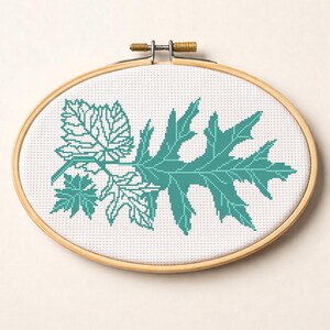 May include: An oval cross-stitch embroidery featuring a teal leaf design. The leaves are stitched on white fabric, set within a wooden embroidery hoop. The design includes several leaf shapes, showcasing detailed patterns.