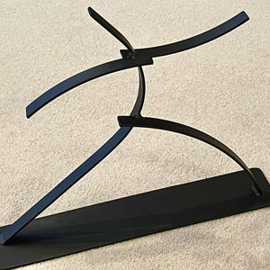 May include: Black metal sculpture depicting a stylized figure in motion. The sculpture features curved lines and a rectangular base, creating a modern and abstract aesthetic. The artwork is suitable for home or office decor.