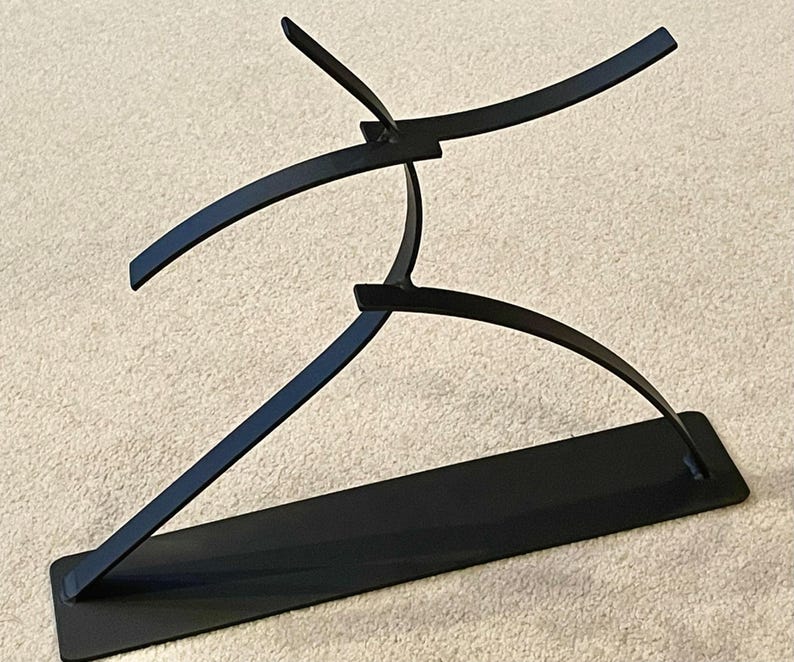 May include: Black metal sculpture depicting a stylized figure in motion. The sculpture features curved lines and a rectangular base, creating a modern and abstract aesthetic. The artwork is suitable for home or office decor.