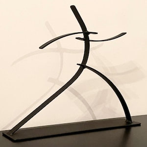 May include: A black metal sculpture depicting a stylized human figure in motion. The sculpture has a minimalist design with curved lines and a rectangular base. The figure's arms are outstretched, and its legs are bent, suggesting movement.