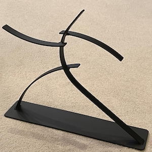 May include: A black metal sculpture depicting a stylized human figure in motion. The sculpture has a rectangular base and curved, flowing lines suggesting movement. The artwork is minimalist and modern, suitable for home decor.