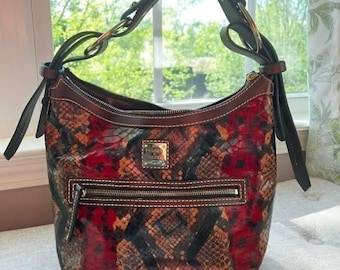 May include: A Dooney & Bourke handbag with a snakeskin pattern in red, brown, and black. The shoulder bag has a zip closure, a front pocket, and a brown leather handle. The bag has a gold-tone metal logo and hardware.
