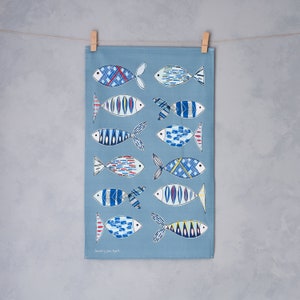 May include: A blue tea towel with a pattern of stylized fish in shades of blue, red, and yellow. The fish have geometric patterns and are arranged vertically down the towel. The text "Designed by Jane Bowler" is printed at the bottom of the towel.