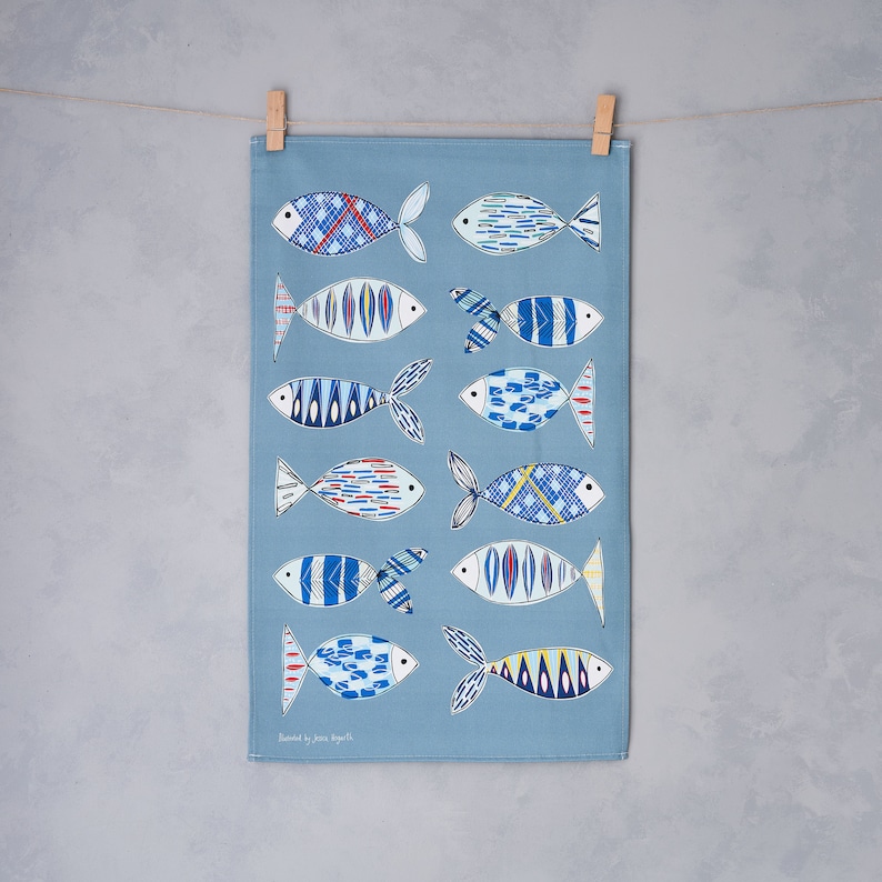 May include: A blue tea towel with a pattern of stylized fish in shades of blue, red, and yellow. The fish have geometric patterns and are arranged vertically down the towel. The text "Designed by Jane Bowler" is printed at the bottom of the towel.
