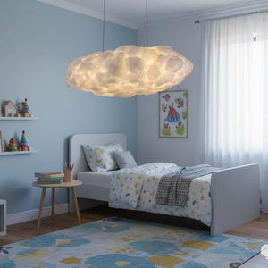 May include: A cloud-shaped pendant light illuminates a child's bedroom. The room features a bed, artwork, and a rug with a blue and yellow pattern. The walls are painted a light blue, creating a calming atmosphere. The light fixture is the focal point.