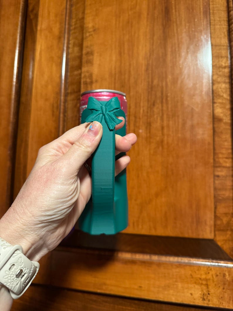 Puede incluir: Un enfriador de latas de color verde azulado con un dise&ntilde;o de lazo. El enfriador est&aacute; dise&ntilde;ado para contener una lata de bebida de tama&ntilde;o est&aacute;ndar. El lazo est&aacute; en la parte superior del enfriador y el asa es de color verde azulado s&oacute;lido.