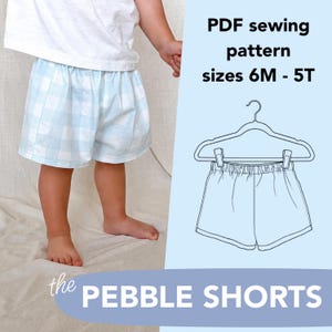 May include: A PDF sewing pattern for the Pebble Shorts in sizes 6M to 5T. The image displays a pair of light blue and white gingham shorts with an elastic waistband, alongside a line drawing of the shorts on a hanger and the text PDF sewing pattern sizes 6M - 5T and the Pebble Shorts.