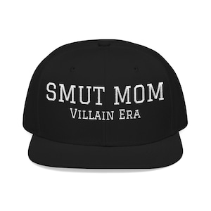 May include: Black baseball cap featuring the white text "SMUT MOM" above "VILLAIN ERA". The cap has a flat brim and a structured crown, typical of a baseball cap.