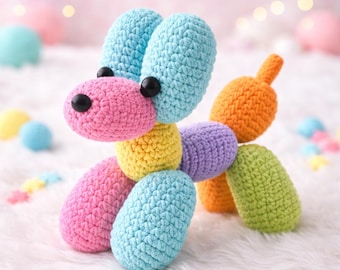 May include: A colorful, handmade crochet dog in a balloon animal style. The dog features blue, pink, yellow, purple, orange, and green sections, with black button eyes. The toy is set against a soft, white background.