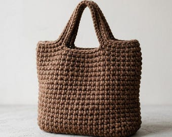 May include: A medium brown tote bag crafted with a thick, textured crochet knit pattern. The bag features a rectangular body with a flat base and two integrated, sturdy handles at the top, showcasing a consistent, dense stitch throughout the design.