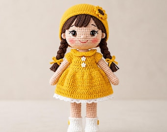 Puede incluir: Una muñeca de ganchillo hecha a mano con cabello castaño oscuro en dos trenzas, que lleva una boina amarilla con un girasol, un vestido amarillo con dos pequeños botones de flores blancas, un dobladillo de encaje blanco y botas blancas.