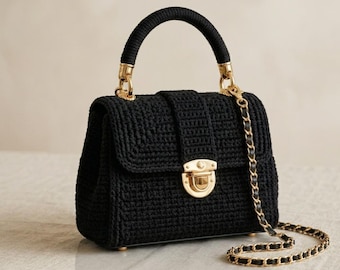May include: Black crochet handbag with a gold-tone chain strap and hardware. The bag features a top handle and a flap closure with a gold clasp. The bag is a structured design, suitable for various occasions.