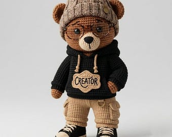 Puede incluir: Un oso de peluche de ganchillo marrón que lleva un gorro de punto beige, gafas redondas y una sudadera negra con capucha con la palabra CREATOR bordada en un parche beige. El oso lleva pantalones cargo beige y zapatillas negras y beige.