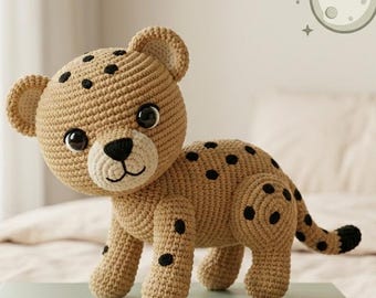 May include: A crocheted toy cheetah in tan with black spots. The cheetah has a cream-colored face, large black eyes, and small ears. The tail is black at the tip. The toy is approximately 10 inches long.