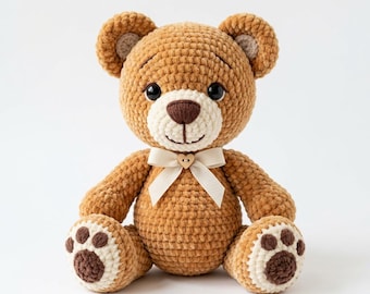 Puede incluir: Un oso de peluche tejido a ganchillo con hilo marrón suave, con hocico e interior de las orejas de color crema. Tiene ojos de plástico negro, una nariz bordada en marrón oscuro y una cinta crema atada al cuello con un pequeño botón de madera en forma de corazón.