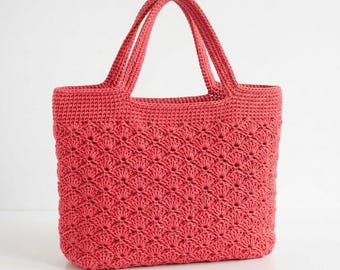Puede incluir: Un bolso tote de ganchillo color coral que presenta un patrón de punto de concha texturizado en todo el cuerpo, una base plana sólida y dos asas resistentes a juego unidas al borde superior, ofreciendo un diseño abierto estructurado y flexible.