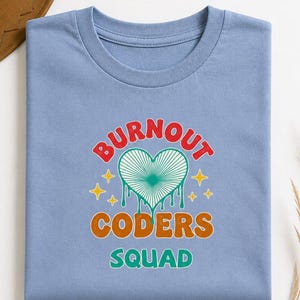 May include: A light blue crew neck t-shirt featuring a graphic print with the text "BURNOUT CODERS SQUAD". The design includes a central heart with radiating lines and dripping edges, surrounded by four yellow four-pointed stars in a retro style.