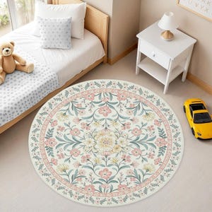 May include: A round area rug featuring a cream-colored background with a symmetrical floral pattern in shades of soft pink, muted green, and pale yellow. The design includes a central flower motif surrounded by intricate botanical vines and leaves.