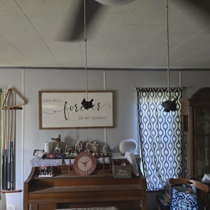 Könnte beinhalten: Ein Raum mit einem Klavier, Vorhängen und einem Schild mit der Aufschrift "You will forever be my always". Eine Uhr und andere dekorative Gegenstände befinden sich auf dem Klavier. Zwei dekorative Hängeobjekte sind von der Decke abgehängt.