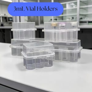 May include: A collection of clear, rectangular plastic 3mL vial holders with molded interior compartments. The containers feature stackable lids and transparent walls, designed to organize small laboratory vials with colored caps securely.
