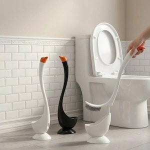 May include: Swan-shaped toilet brush and holder set. The set includes a white brush with an orange accent, a black holder, and a white holder. The brush is being held near a white toilet.