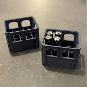May include: Two gray miniature crates, one filled with four black and red AA batteries. The crates have a rectangular shape with arched openings and window-like details. The crates are made of a solid material.