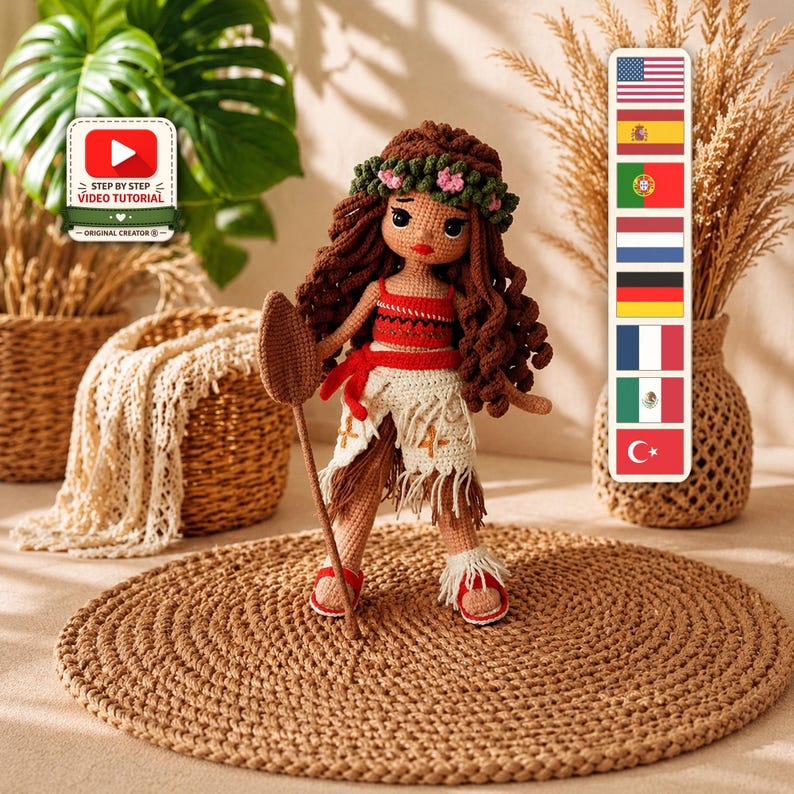 Moana amigurumi crochet doll with long curly brown hair, a green flower crown with pink flowers, a red top, a white fringed skirt, red sandals and a handmade wooden paddle.