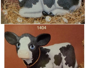 May include: Two black and white ceramic cow figurines. The first is a lying down calf with black spots on a white background. The second is a standing calf with white spots on a black background. The standing calf has a gold bell around its neck.