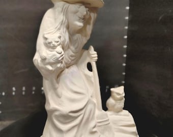 May include: A cream-colored ceramic witch figurine holding a cat and a broom. The witch wears a pointed hat and a long dress. An owl sits on a small rock next to the witch. The figurine is on a round base.