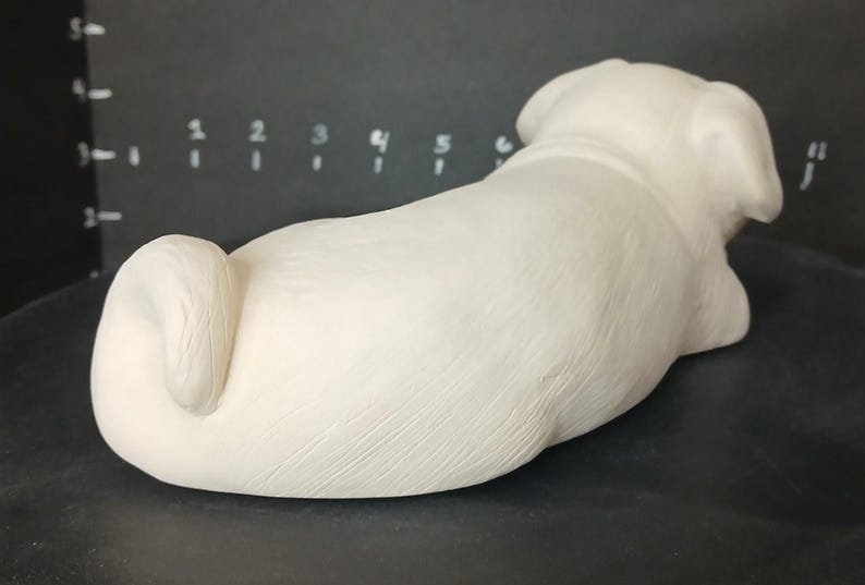 May include: White ceramic pug dog sculpture in a lying down position. The sculpture has a smooth, textured surface.
