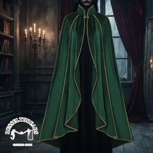 May include: A floor-length emerald green cape featuring a high collar, gold trim along the edges, and a silver metal clasp at the neckline. The garment is worn over a solid black base layer, creating a structured silhouette with flowing fabric.