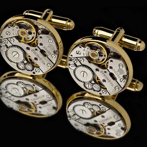 May include: Gold cufflinks with a round, silver face featuring a detailed clock mechanism. The face of the cufflinks has the text "21 камень" and "20095".