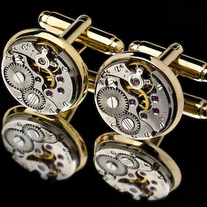 May include: Gold cufflinks with a round, silver face featuring a detailed, exposed clockwork mechanism. The clockwork is visible through the face of the cufflinks.