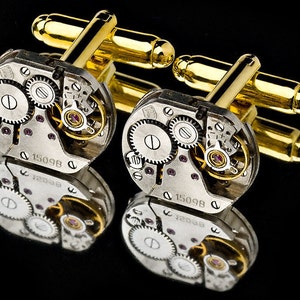 May include: A pair of gold cufflinks with a silver watch mechanism design. The cufflinks feature a circular watch face with visible gears and the text "1509B".