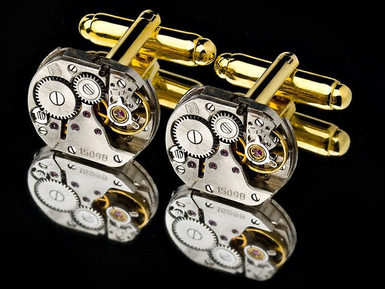 May include: A pair of gold cufflinks with a silver watch mechanism design. The cufflinks feature a circular watch face with visible gears and the text "1509B".