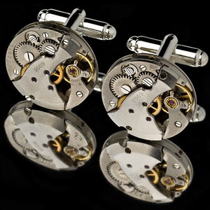 May include: A pair of silver cufflinks with a circular design featuring exposed watch gears and the year 2009 engraved on each cufflink.