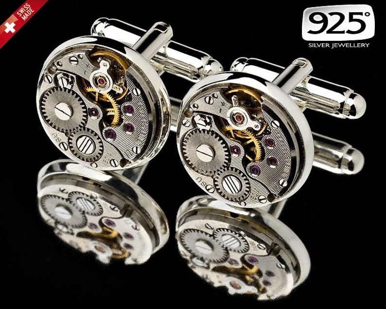 May include: Pair of silver cufflinks with a watch mechanism design. The cufflinks feature visible gears, ruby-colored jewels, and the text "925 Silver Jewellery". The Swiss Made logo is visible in the upper left corner.