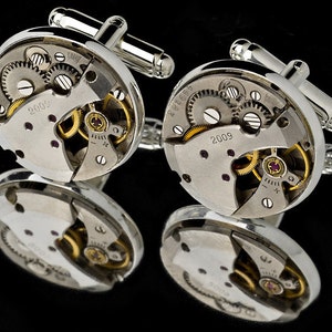 Puede incluir: Gemelos de plata con un dise&ntilde;o circular que presenta engranajes de reloj expuestos y el a&ntilde;o 2009 impreso en la cara.