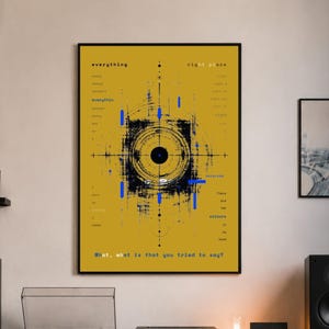 May include: A framed yellow art print with black and blue abstract design and text. The print hangs on a white wall above a record player, stereo, and vinyl record storage. A black leather chair and guitar are also visible.
